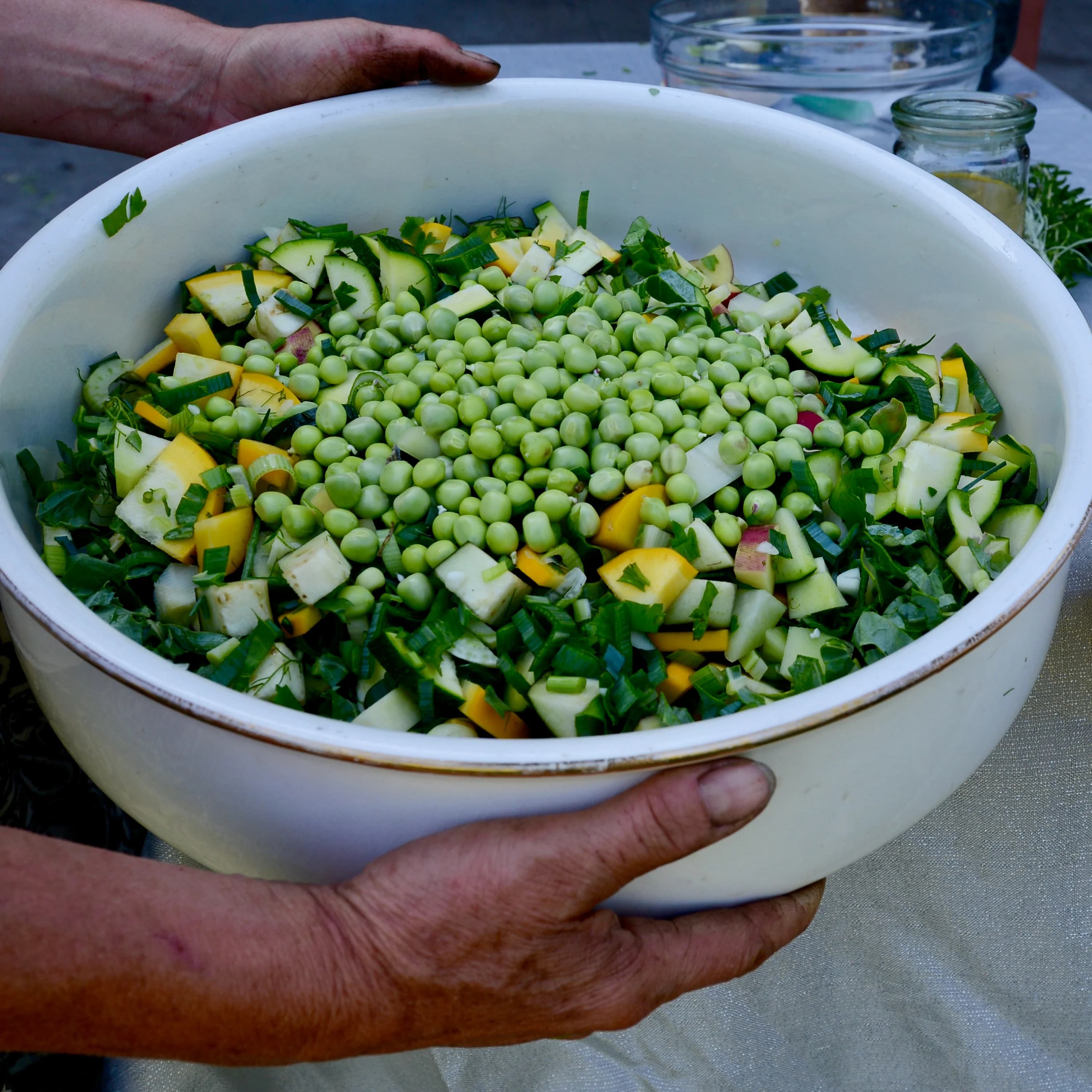 Kom met verse doperwten, courgette en kruiden, vastgehouden door gerimpelde handen